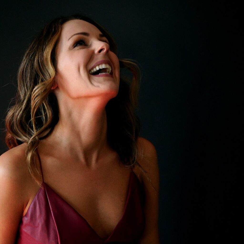 Joyful woman in a red dress, laughing confidently against a dark background