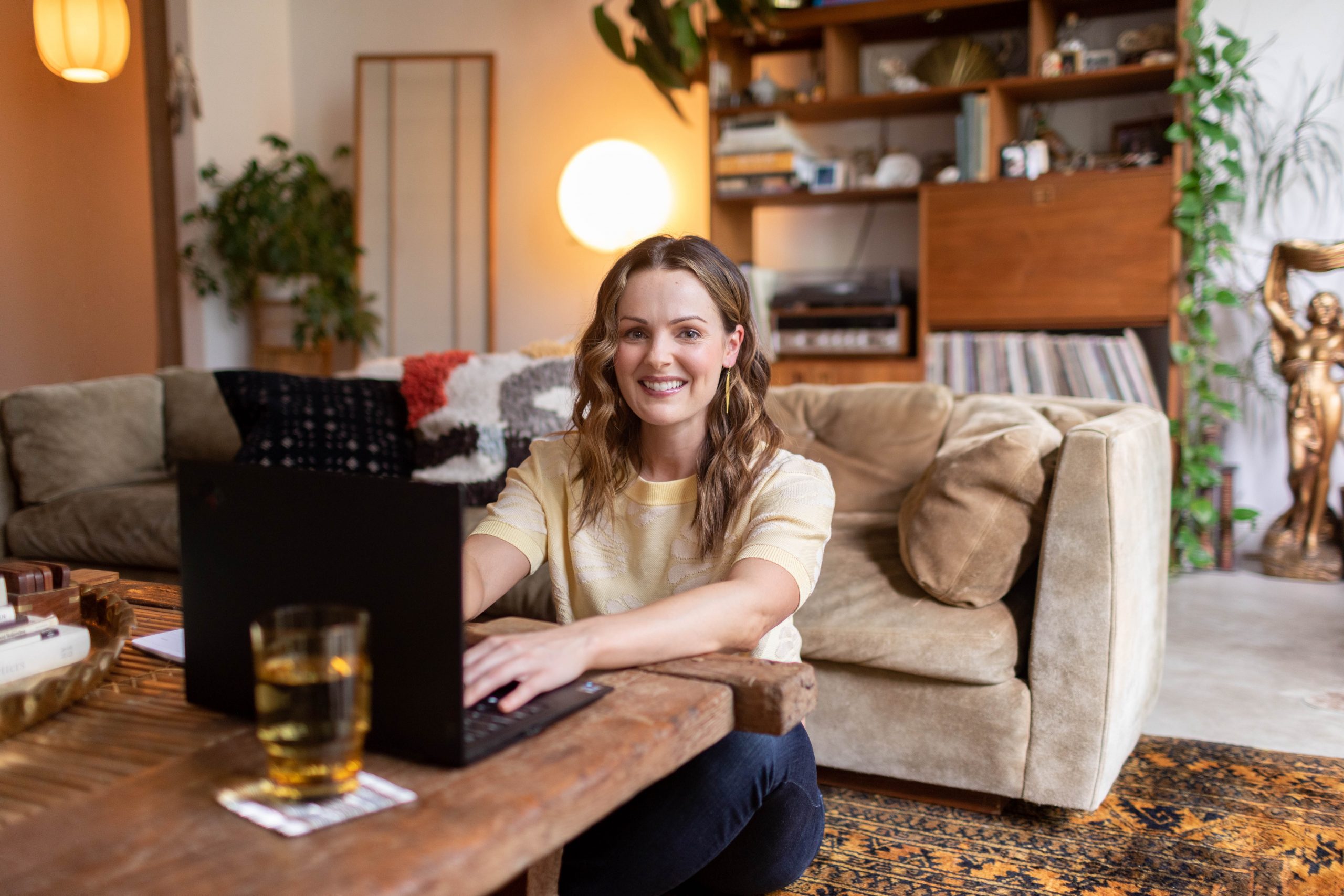 Smiling woman working on a laptop in a cozy living room with warm decor